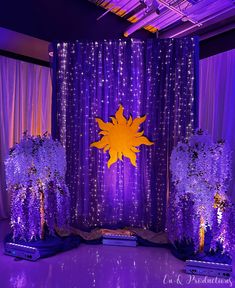 a purple and yellow stage set up for a party with flowers, trees, and lights