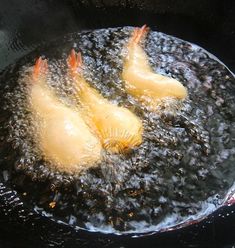 three pieces of food cooking in a frying pan on the stove top with water