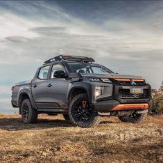 a grey truck parked on top of a grass covered hill next to the ocean and clouds