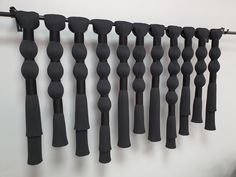 a bunch of black rods hanging on a wall next to a white wall and a metal hook