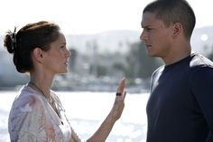 a man and woman standing next to each other near the water looking at each other