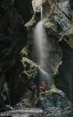 a woman sitting on top of a rock next to a waterfall