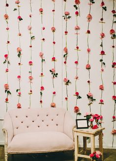 a pink couch sitting in front of a white wall with flowers hanging from it's sides