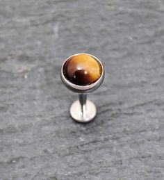 Natural 5mm Tiger's Eye gem set in a polished 316l steel labret.  Did you know that Tigers Eye's are seen as the astrological birthstone for Gemini's? Tiger eye is seen to be a stone that enhances the strength of conviction, convenience, safety, courage, self-esteem and confidence in ones own power.  It is also known as a solar plexus chakra Listing is for a single labret. DETAILS ---------------------------------------------------- The Tiger's Eye crystal is a 5mm round cabochon, and sits in a Internally Threaded Surgical Steel Piercings, Silver Stainless Steel Piercings, Nickel-free Stainless Steel Round Piercings, Nickel-free Round Stainless Steel Piercings, Hypoallergenic Stainless Steel Round Piercings, Piercings Lobe, Tiger's Eye Crystal, Tigers Eye Gem, Tiger Eye Crystal