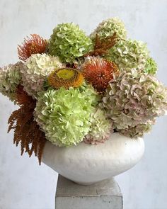 a vase filled with lots of green and red flowers on top of a white pedestal