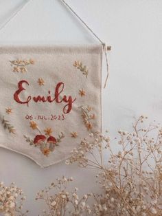 an embroidered banner hanging on a wall next to some dried flowers and plants with the word family printed on it