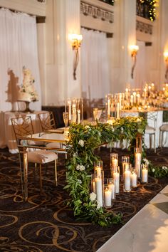 a long table with candles and greenery on it in the middle of a room