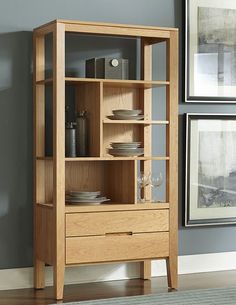 a wooden bookcase with glassware and plates on it in front of a gray wall