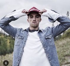 a man in a denim jacket is holding his hat over his head and looking at the camera