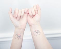 two hands with small tattoos on them holding each other's palms up in the air