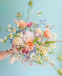 a bouquet of flowers is being held by someone's hand on a blue background