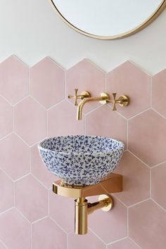 a blue and white bowl sitting on top of a gold faucet next to a mirror