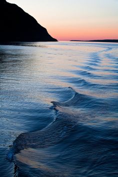 the sun is setting over the ocean with waves coming in to shore and mountains in the distance