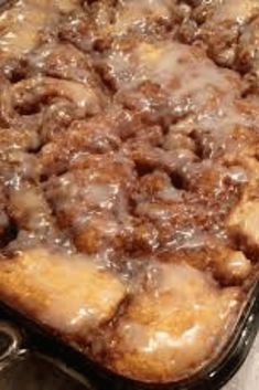 a close up of a cake in a pan with icing and cinnamon rolls on top