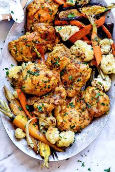 a white plate topped with chicken, carrots and cauliflower covered in herbs