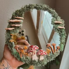 a hand holding up a mirror with mushrooms and moss growing on the surface in front of it