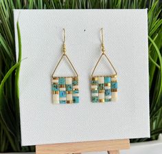 a pair of earrings sitting on top of a wooden stand next to a potted plant