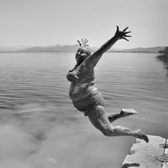 a man jumping into the water with his arms in the air while wearing shorts and socks