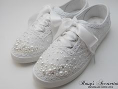 a pair of white tennis shoes with pearls on the side and bows at the top