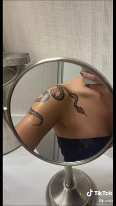 a woman's reflection in a mirror with snake tattoos on her arm and shoulder