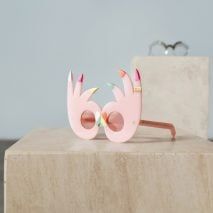 a pair of pink flamingo glasses sitting on top of a block of concrete with sunglasses in the background