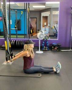 a woman is sitting on the floor in a gym doing squats with her arms behind her back