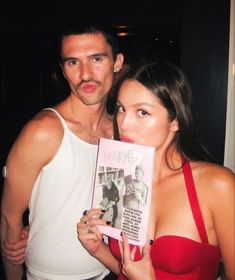 a man standing next to a woman holding up a pink book in front of her