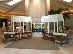 an indoor wedding venue with white drapes and wooden wagon tables set up for the ceremony