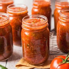 several mason jars filled with tomato sauce on top of a wooden table next to tomatoes