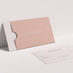 a pink business card sitting on top of a white table next to a piece of paper