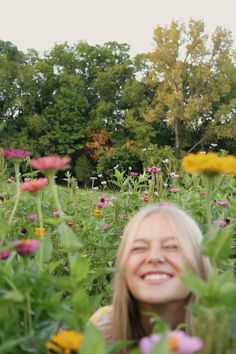 a woman standing in the middle of a field full of flowers smiling at the camera