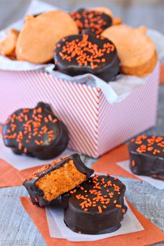 chocolate covered cookies and orange sprinkles in a pink box on top of an orange napkin