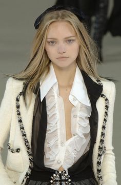 a model walks down the runway wearing a white jacket and black pants with ruffles