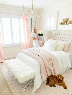 a woman standing next to a bed in a room with pink curtains and white furniture