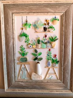 a frame with some flowers and plants in it on the wall next to a potted plant