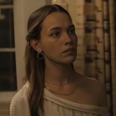 a woman with long hair in a white shirt looking off to the side and wearing large earrings