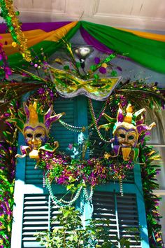 two mardi gras masks hanging from the side of a building with green shutters