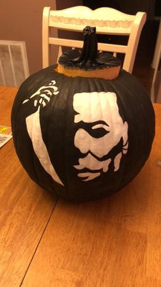 a black and white pumpkin with a face painted on it sitting on top of a wooden table