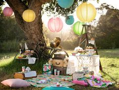 an outdoor picnic with paper lanterns and tea cups on the grass, near a tree