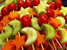 fruit and vegetable skewers are arranged on sticks in a platter with cherry tomatoes, cucumbers, carrots, and lettuce