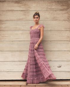 a woman standing in front of a wooden wall wearing a dress with ruffles