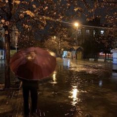 a person with an umbrella walking in the rain on a city street at night time