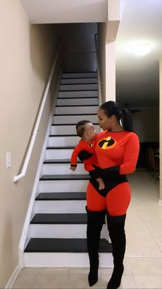 a woman holding a baby wearing an orange and black costume while standing next to stairs