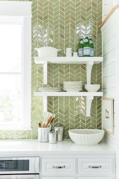 a kitchen with green and white tiles on the wall next to a shelf filled with utensils