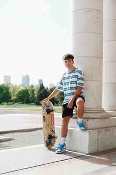 a young man holding a skateboard sitting on the side of a stone pillar in front of a building