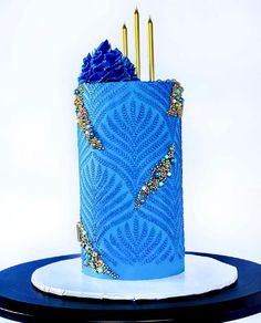 there is a blue cake with gold decorations on the top and two candles in the middle