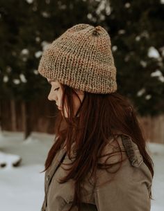 a woman with long hair wearing a brown knitted hat standing in the snow outside