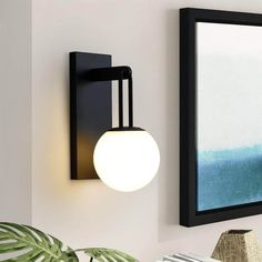 a wall mounted light next to a mirror on the wall with a plant in front of it