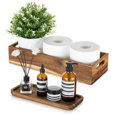 a wooden tray with two bottles and three candles on it next to a potted plant