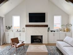 a living room with white furniture and a flat screen tv mounted above the fire place